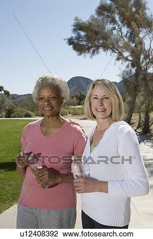 Stock Image - Senior women stand with bottles of mineral water. Fotosearch