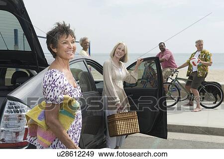 Stock Photo - Senior women unpack car observed by men on bicycles. Fotosearch