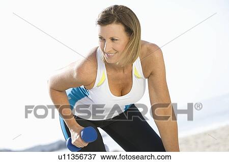 Stock Photo - Sporty woman at the beach lifting hand weights. Fotosearch
