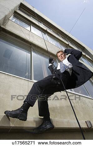 Stock Image - Spy Rappelling and Using Cell Phone. Fotosearch