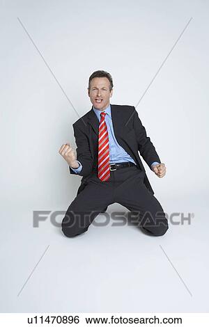Stock Photograph - Studio portrait of businessman kneeling and punching air. Fotosearch