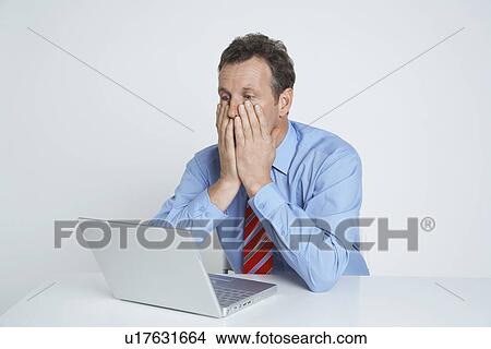 Studio shot of businessman with head in hands using laptop View Large Photo Image Picture - Studio shot of businessman with head in hands using laptop. Fotosearch