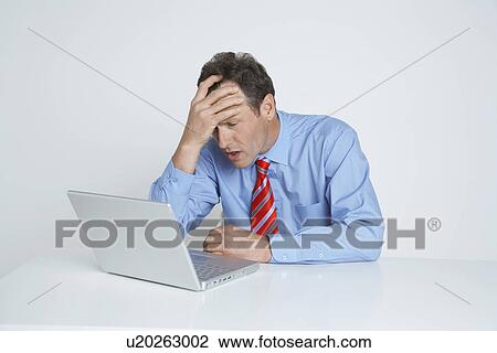 Stock Image - Studio shot of businessman with head in hands using laptop. Fotosearch