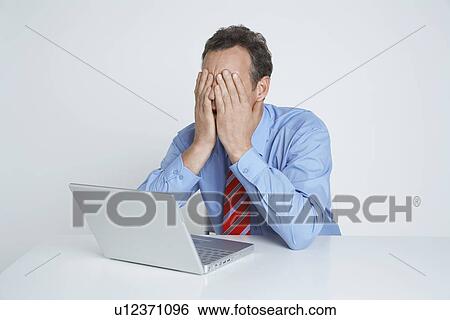Stock Photograph - Studio shot of businessman with head in hands using laptop. Fotosearch
