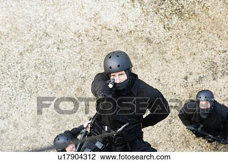 Stock Image - SWAT Team Officer Rappelling and Aiming Gun. Fotosearch