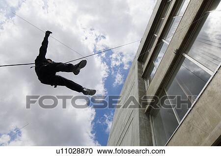 Stock Image - SWAT Team Officer Rappelling from Building. Fotosearch