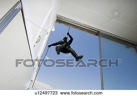Stock Image - SWAT Team Officer Rappelling from Building. Fotosearch