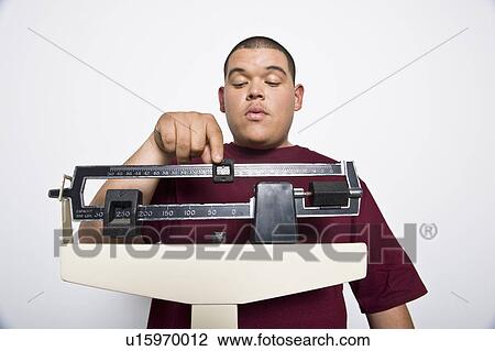 Stock Image - Teenage (16-17) boy using weight scales. Fotosearch