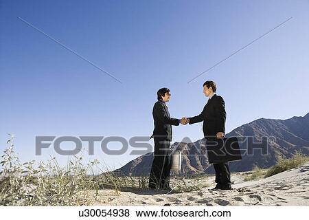 Stock Photo - Two Businessmen Shaking Hands in the Desert. Fotosearch