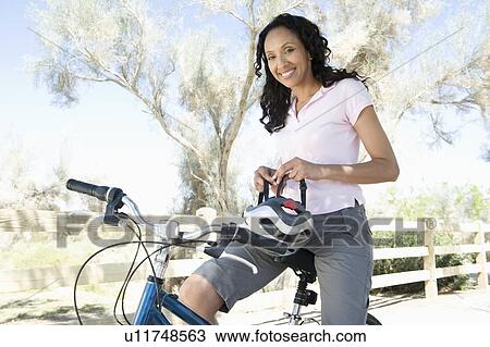 Stock Image - Woman adjusts cycling helmet on mountain bike. Fotosearch