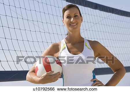 Stock Photograph - Woman at beach volleyball net with ball. Fotosearch