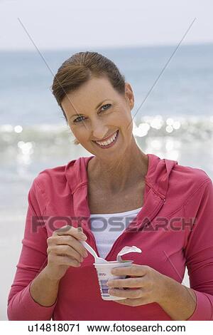 Stock Image - Woman eating yoghurt on beach. Fotosearch