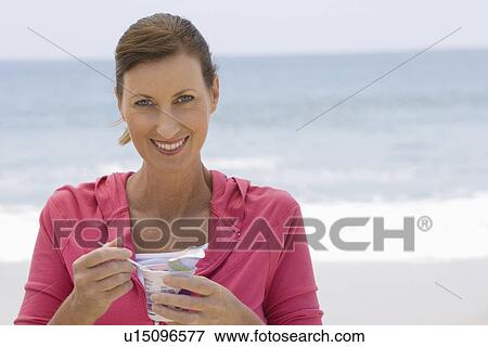 Stock Photo - Woman eating yoghurt on beach. Fotosearch