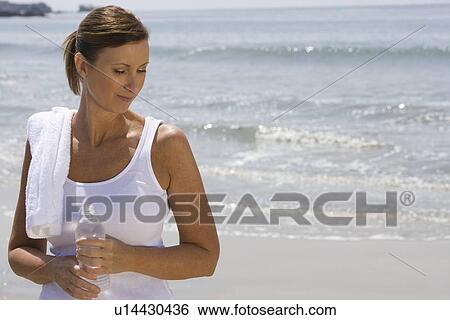 Stock Photograph - Woman holding bottle of water at the beach. Fotosearch