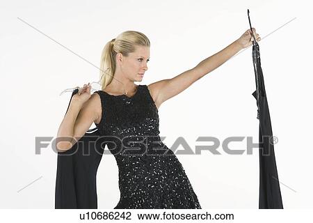 Stock Image - Woman holds up black dress, choosing what to wear. Fotosearch