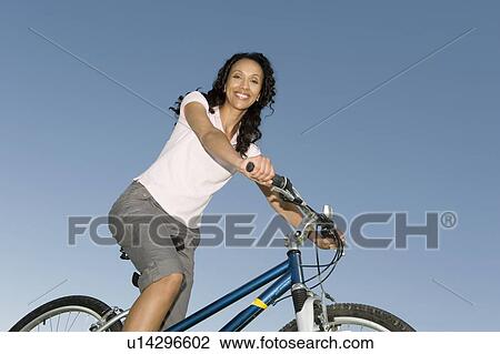 Stock Image - Woman sits on mountain bike against clear blue sky. Fotosearch