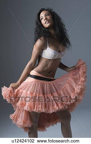 Stock Image - Woman stands in lace bra and peach coloured petticoat skirt. Fotosearch
