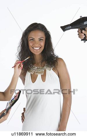 Stock Image - Woman stands in white dress with stylists on hand. Fotosearch