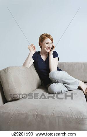 Stock Image - Woman talking on mobile phone on sofa. Fotosearch