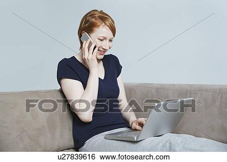 Woman using laptop and mobile phone on sofa View Large Photo Image Stock Photograph - Woman using laptop and mobile phone on sofa. Fotosearch