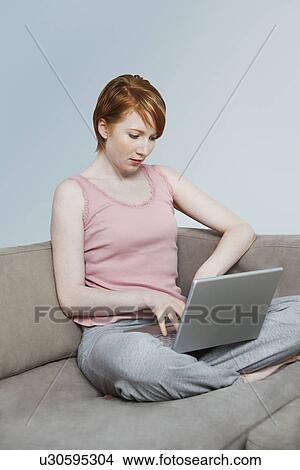 Picture - Woman using laptop on sofa. Fotosearch