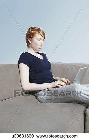 Stock Image - Woman using laptop on sofa. Fotosearch
