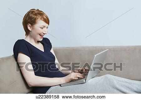 Stock Photo - Woman using laptop on sofa. Fotosearch