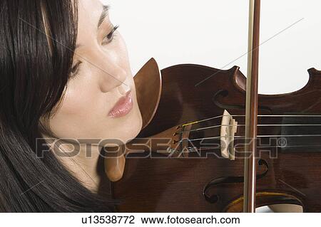 Stock Image - Young Asian woman concentrates on playing the violin. Fotosearch