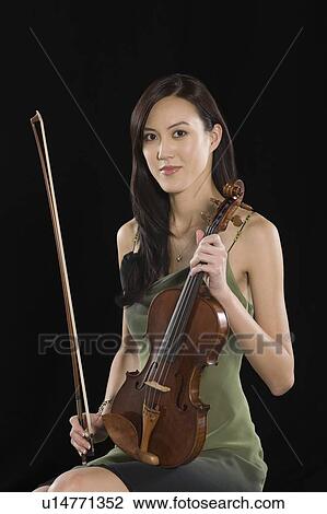 Stock Image - Young Asian woman sits holding a violin. Fotosearch