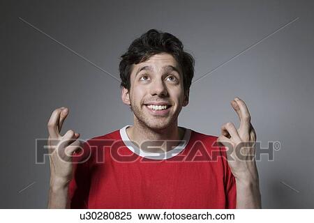 Young man in red top looking up with fingers crossed View Large Photo Image Stock Photography - Young man in red top looking up with fingers crossed. Fotosearch
