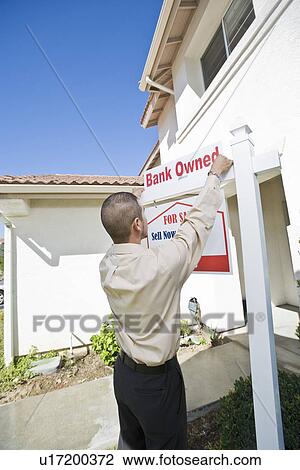 Stock Image - Young man putting up 'for sale notice'. Fotosearch