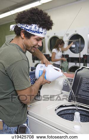 Stock Photo - Young man washing clothes at launderette. Fotosearch