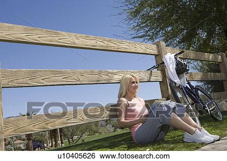 Young woman sits leaning against fence View Large Photo Image Stock Photograph - Young woman sits leaning against fence. Fotosearch