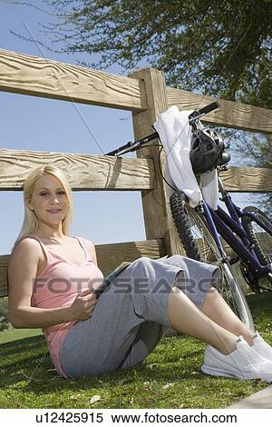 Stock Photography - Young woman sits leaning against fence. Fotosearch