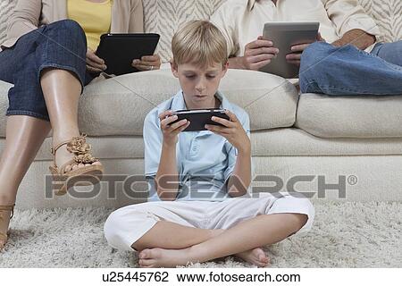 Stock Image - Boy and parents sit with hand-held devices. Fotosearch