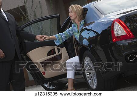 Stock Photography - Chauffeur helps woman from luxury vehicle. Fotosearch