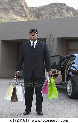 Chauffeur holds shopping bags in driveway near luxury vehicle View Large Photo Image Stock Photo - Chauffeur holds shopping bags in driveway near luxury vehicle. Fotosearch