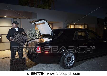 Chauffeur loads suitcases into luxury car at night View Large Photo Image Picture - Chauffeur loads suitcases into luxury car at night. Fotosearch