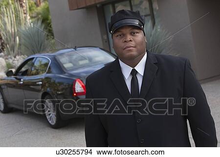 Picture - Chauffeur stands in uniform with luxury vehicle. Fotosearch