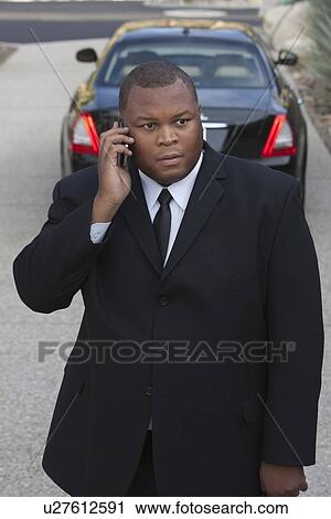 Chauffeur stands on mobile phone with luxury vehicle View Large Photo Image Stock Image - Chauffeur stands on mobile phone with luxury vehicle. Fotosearch