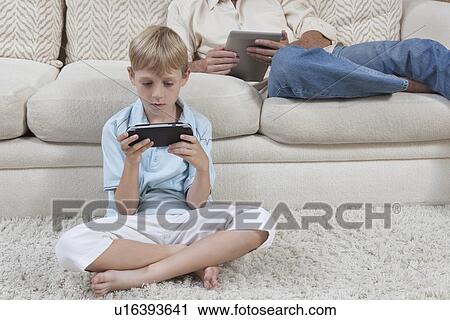 Stock Image - Father and son sit with hand-held devices. Fotosearch