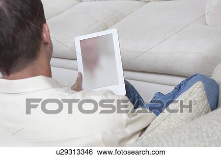Stock Photograph - Man sits reading a digital book. Fotosearch