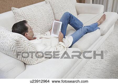 Man sits with feet up reading a digital book View Large Photo Image Picture - Man sits with feet up reading a digital book. Fotosearch