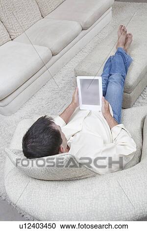 Stock Image - Man sits with feet up reading a digital book. Fotosearch