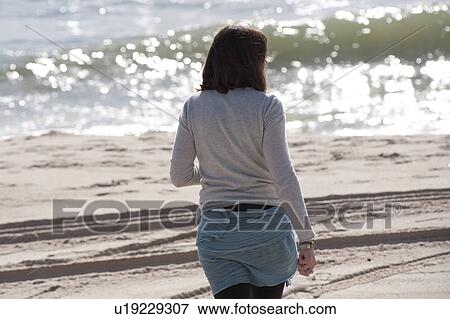 Back view of a woman walking along the beach in the Hamptons View Large Photo Image Stock Photo - Back view of a woman walking along the beach in the Hamptons. Fotosearch