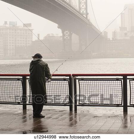 Man fishing on the East River shore in Manhattan, New York City, U. S. A. View Large Photo Image Stock Photo - Man fishing on the East River shore in Manhattan, New York City, U. S. A.. Fotosearch