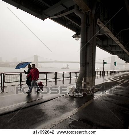 Stock Image - People walking along East River in Manhattan, New York City, U. S. A.. Fotosearch