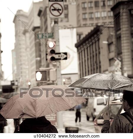 Stock Image - People walking with umbrellas on the streets of Manhattan, New York City, U. S. A.. Fotosearch