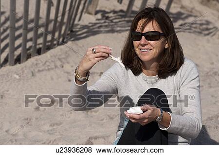 Stock Photo - Woman looking at seashells on the beach in the Hamptons. Fotosearch