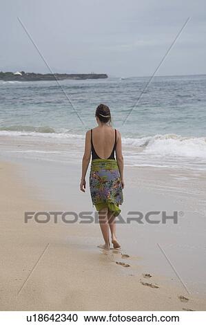 Stock Image - Woman walking along the beach in Bali. Fotosearch